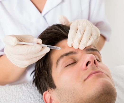 Man with eyes closed getting Botox injection in his forehead