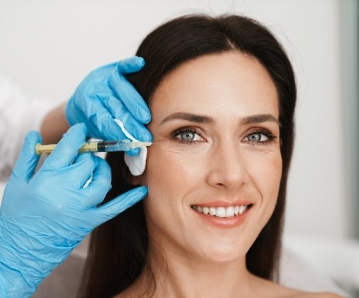 Smiling woman getting Botox injection in wrinkles by her eyes