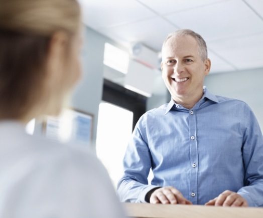 Man in light blue shirt talking to dental team member at front desk