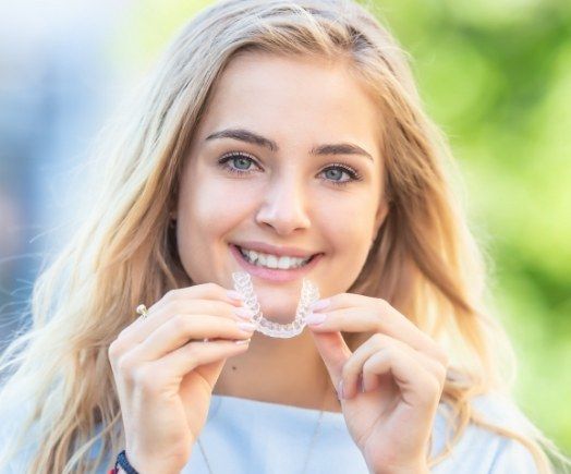 Smiling woman holding Invisalign clear aligner outdoors