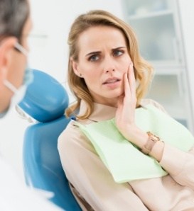 Woman in dental chair holding her jaw in pain