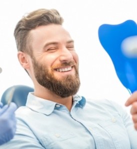 Bearded man in dental chair admiring his smile in mirror