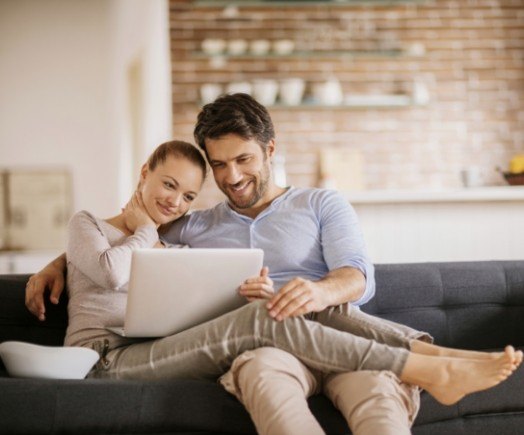 Man and woman cuddling on couch while looking at laptop