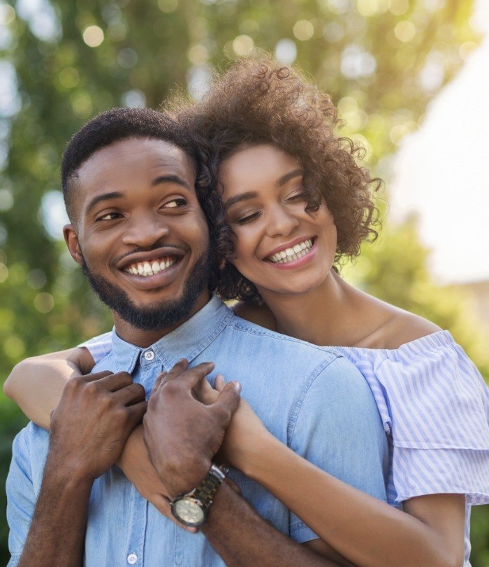 Smiling man and woman hugging outdoors after sedation dentistry in Centennial