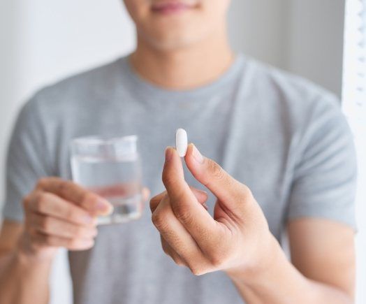 Man holding white pill and glass of water