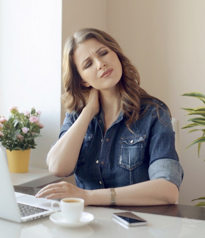 Woman sitting at desk holding jaw in pain needing T M J treatment in Centennial