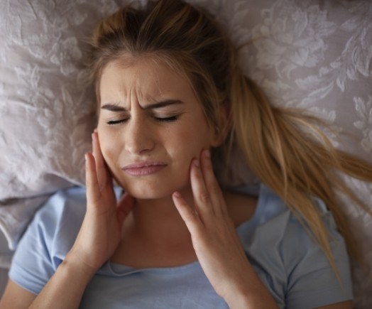Woman laying in bed holding the sides of her jaw in pain