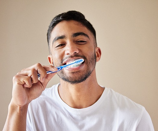 Man in white shirt smiling while brushing his teeth